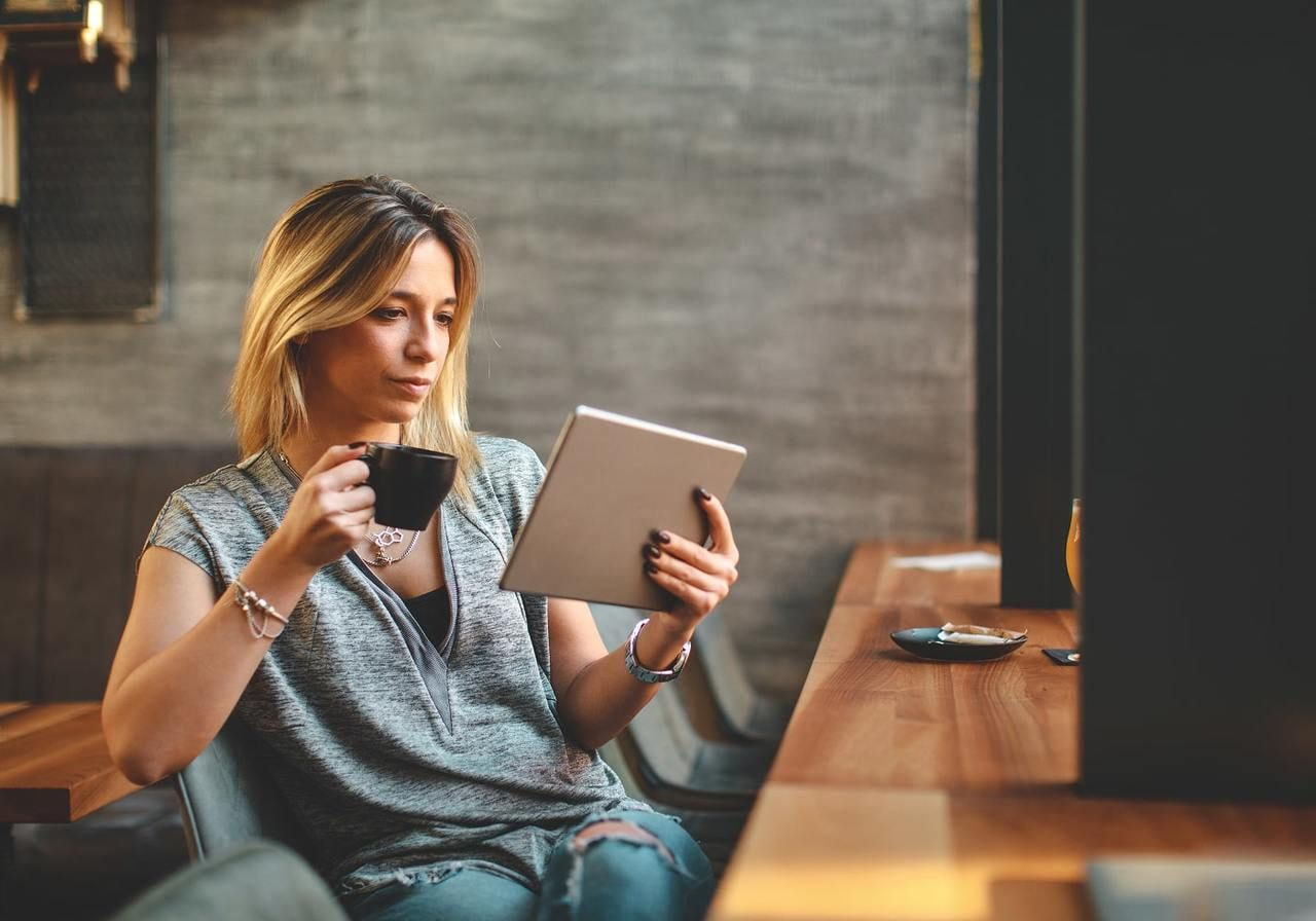 A woman is drinking coffee and using a tablet to find the latest trending products to sell online.